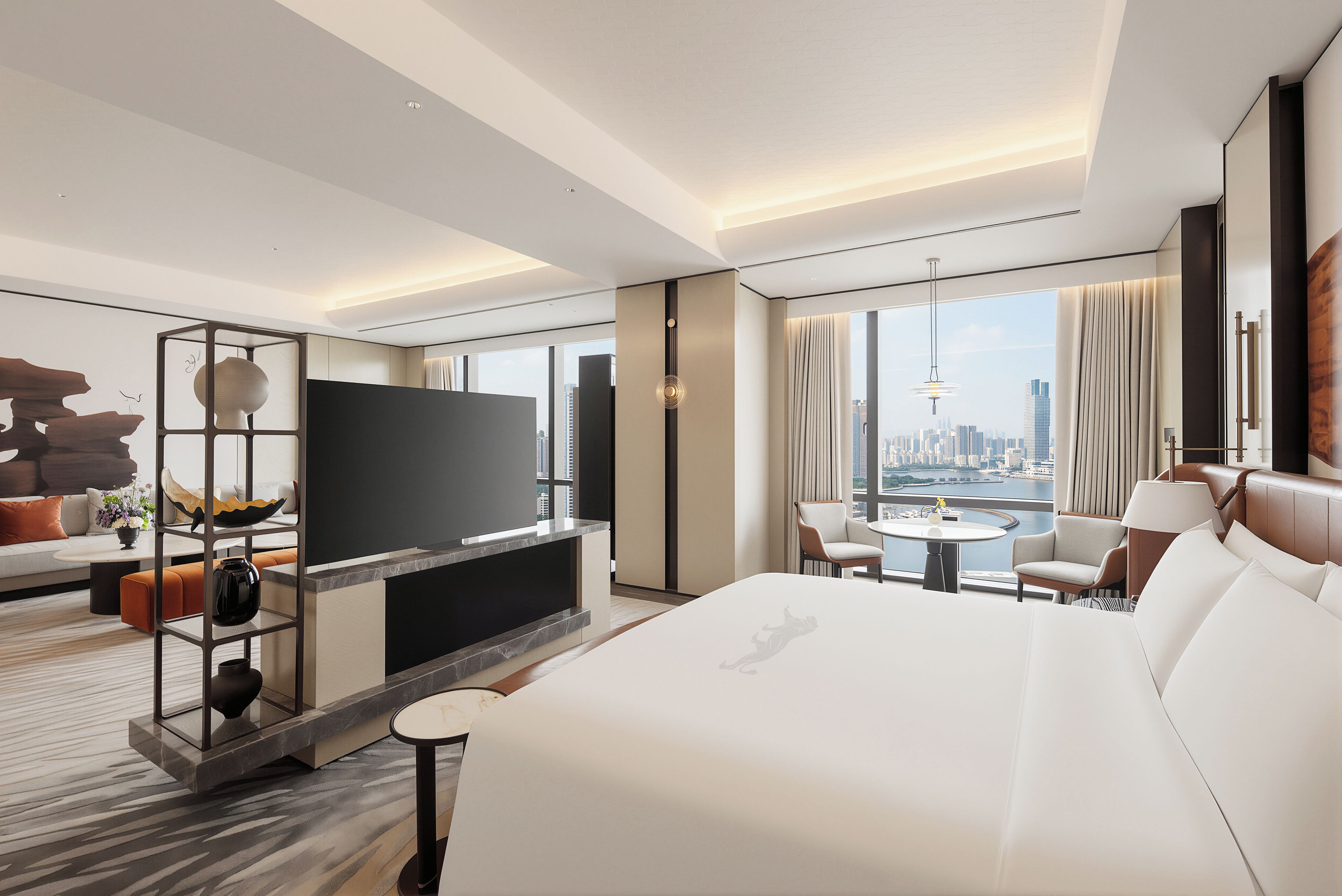 Une chambre d’hôtel moderne dotée d’un grand lit, d’un téléviseur à écran plat, d’un coin salon avec un canapé et des fauteuils, d’une table à manger et offrant une vue sur le paysage urbain grâce à de grandes fenêtres.