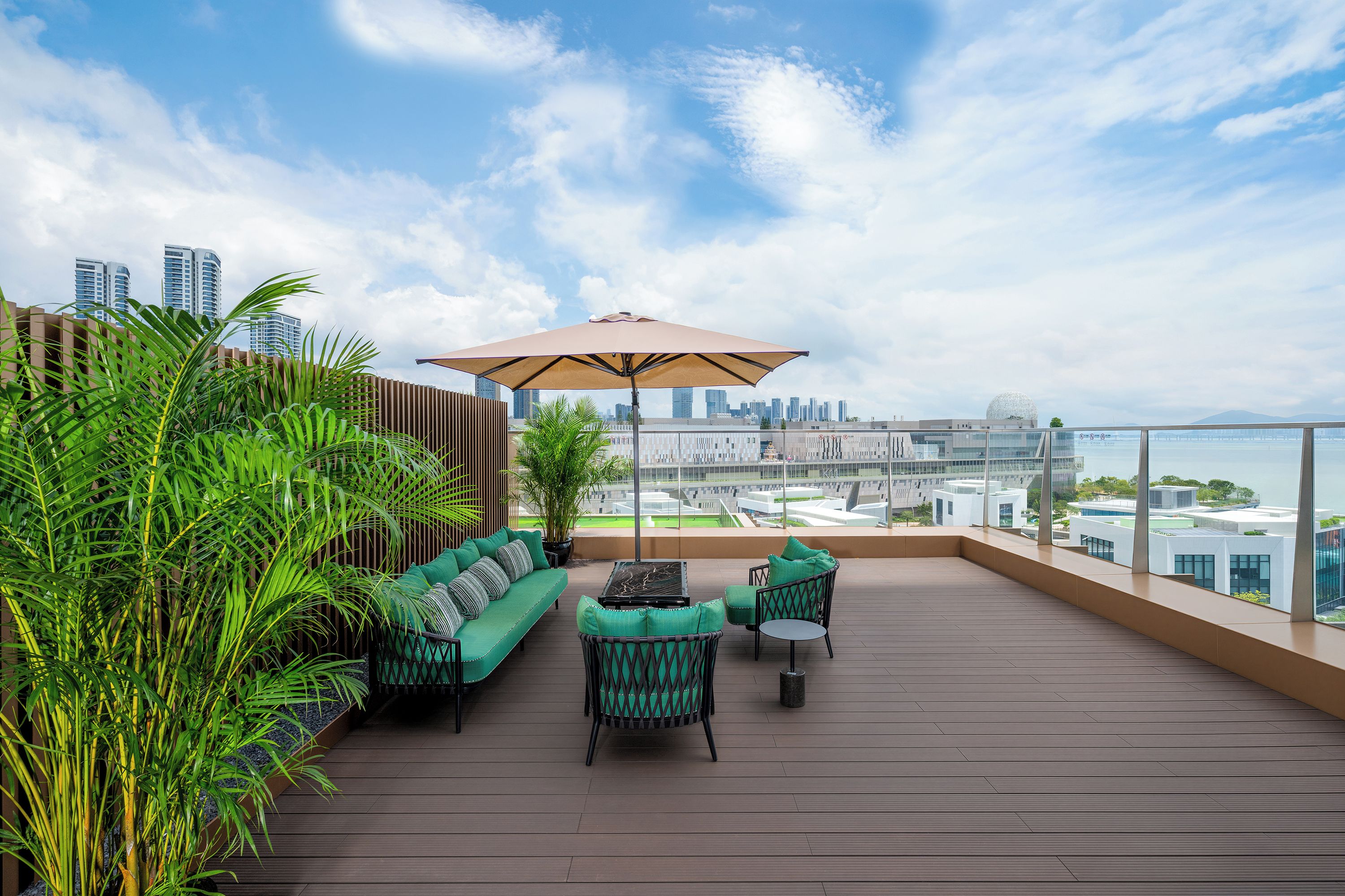 Terraza en la azotea con sofá, sillas y sombrilla, con vistas a un paisaje urbano y al agua.