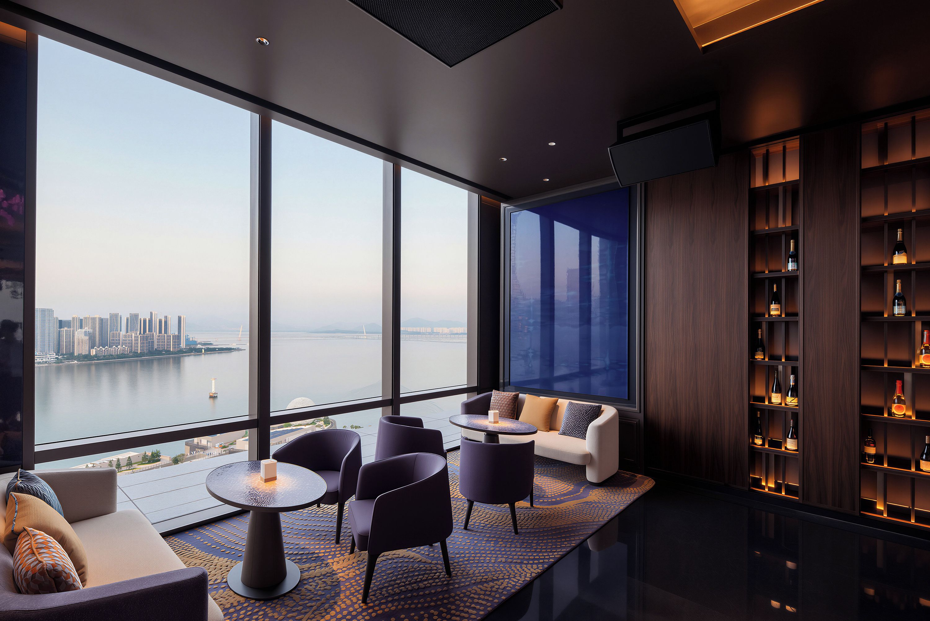 A modern interior with a large window overlooking a cityscape, a seating area with a round table, and a wine rack.