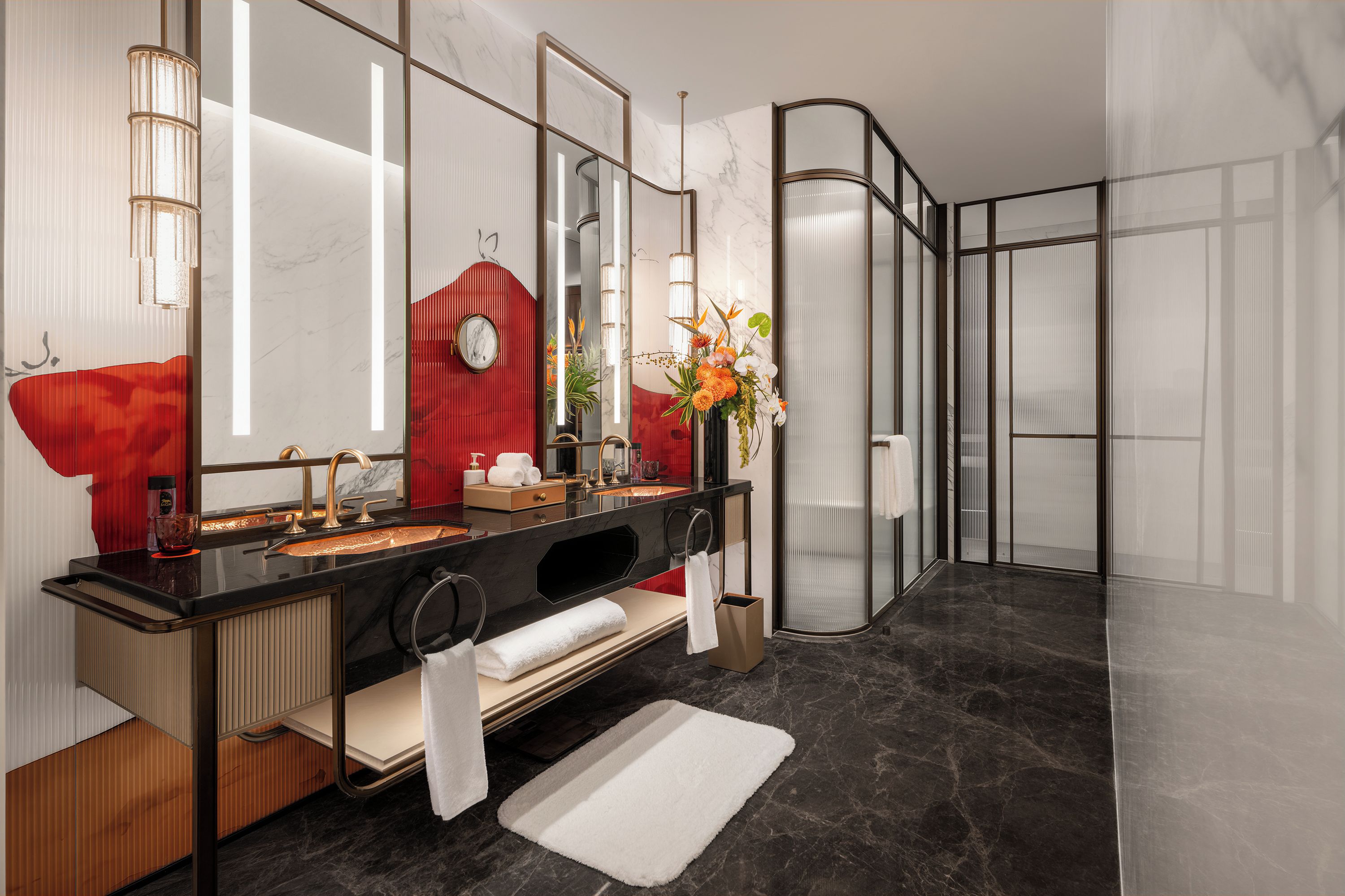 A modern bathroom with a black marble vanity, a red accent wall, a large mirror, and a glass shower enclosure.