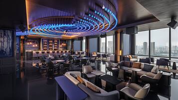 A modern lounge with a curved ceiling light fixture, seating arrangements, and a city view.