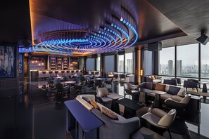 Een moderne lounge met een gebogen plafondlamp, zithoekjes en uitzicht over de stad.