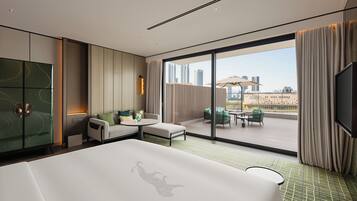 Una habitación de hotel moderna con una cama grande, zona de estar con mesa y balcón con mobiliario exterior.