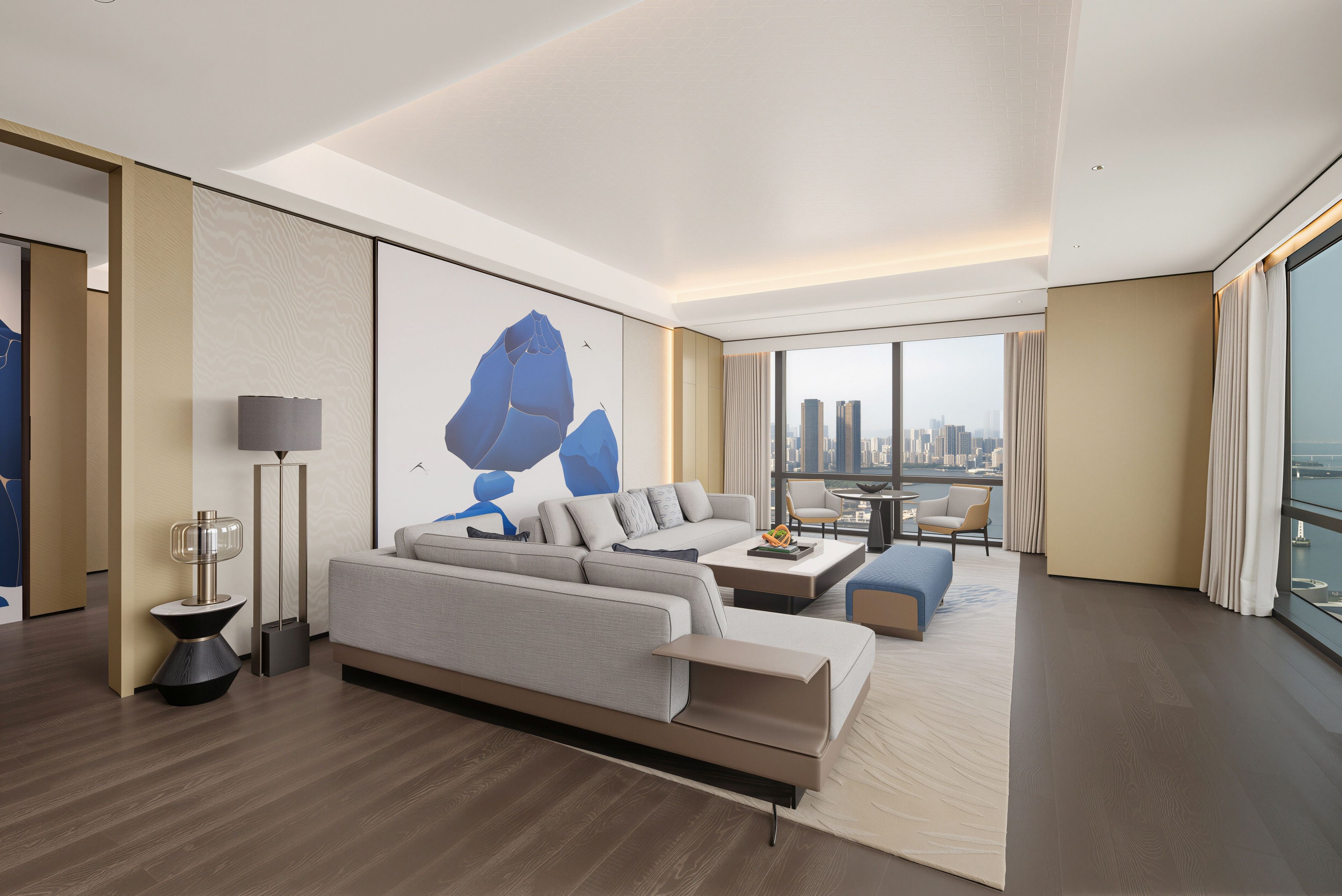 Una habitación de hotel moderna con un sofá grande, una mesa de centro, una lámpara de pie y vistas a la ciudad.