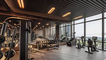 A modern gym with various exercise equipment, large windows, and a view of the city.