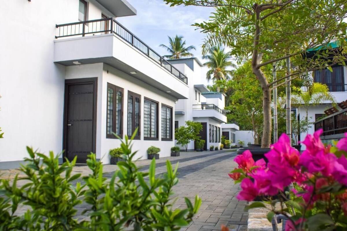 A modern building with a balcony, a paved walkway, and lush greenery.