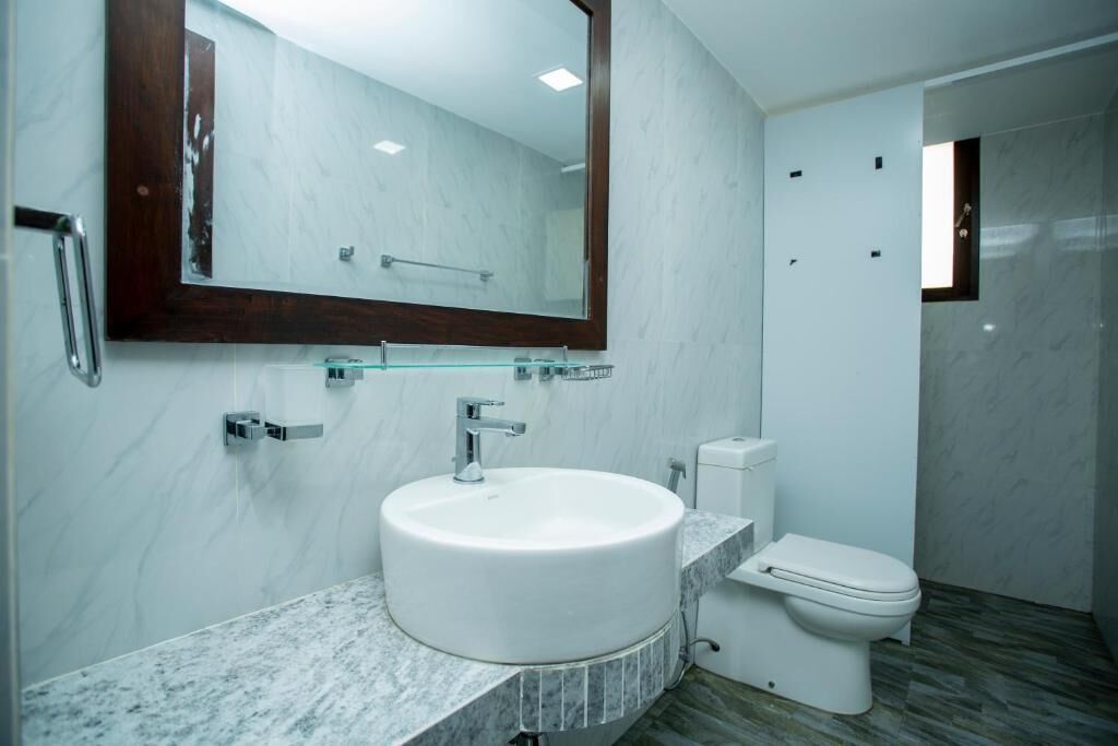 Ein modernes Badezimmer mit Marmorwaschbecken, einer Glasablage, einer Toilette und einem großen Spiegel.