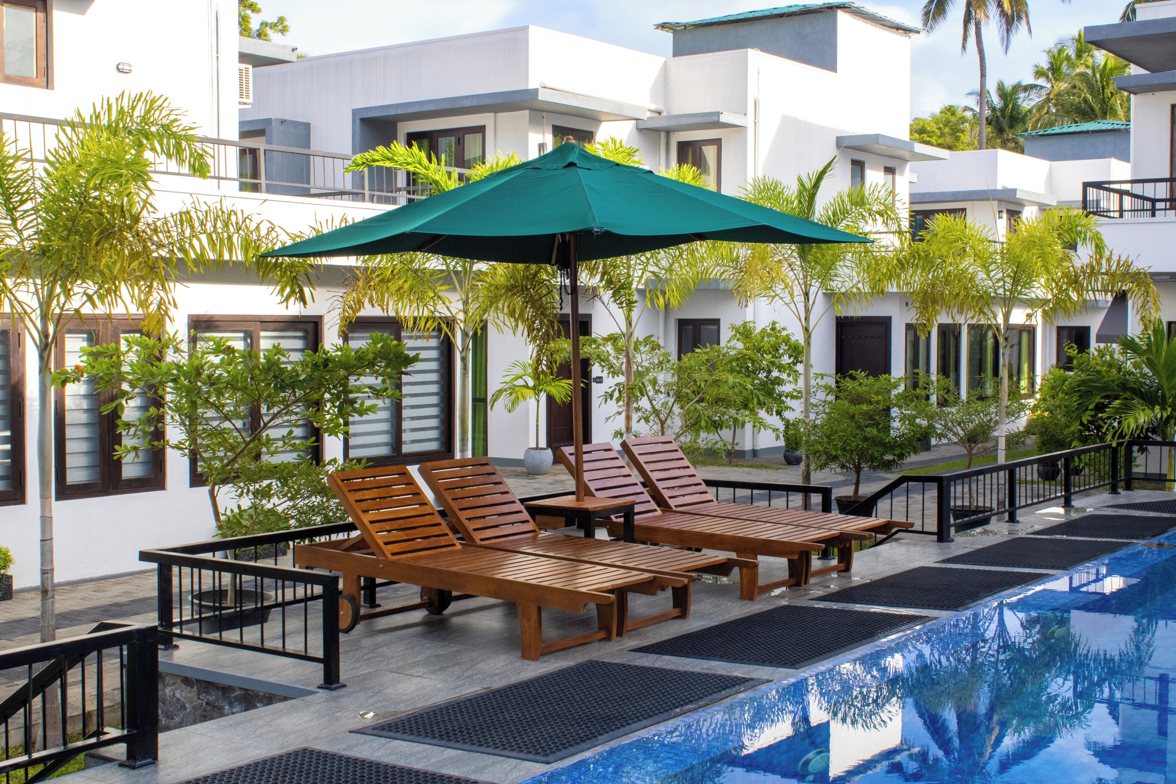 A poolside area with lounge chairs, a table, and a green umbrella.