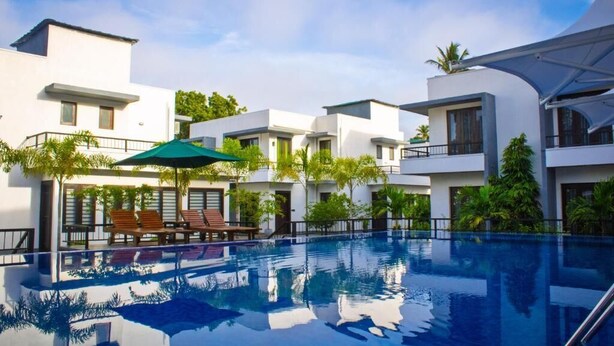 Una piscina con sillones de descanso y sombrillas, rodeada de edificios modernos con balcones y zonas verdes.