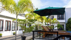 Un patio con un banco de madera, un paraguas verde y plantas en macetas.