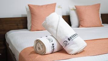 Una cama bien tendida con una toalla enrollada y una almohada, un cabecero de madera y una pared blanca.
