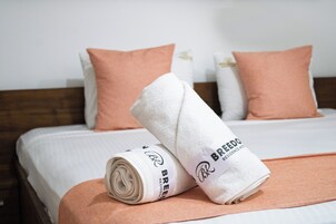 Una cama bien tendida con una toalla enrollada y una almohada, un cabecero de madera y una pared blanca.