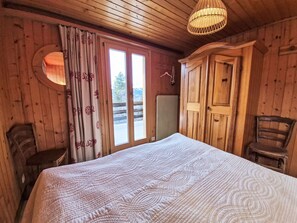 A wooden room with a bed, a chair, a wardrobe, and a window with curtains. - Chalet Le Rhônasson by Interhome (Vercorin)