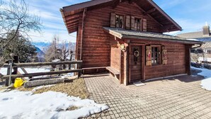 A wooden cabin with a sloped roof, a front porch, and a view of snow-covered mountains. - Chalet Le Rhônasson by Interhome (Vercorin)