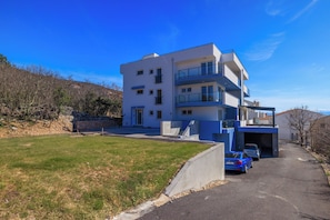 A modern multi-story building with a flat roof, a covered driveway, and a parking area with cars. - Modern apartment with a hot tub, terrace, and ocean view (Dramalj)