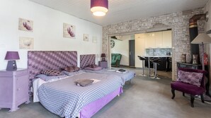 A bedroom with two beds, a stone wall, a kitchenette, and a green chair.