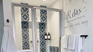 Een badkamer met een douchecabine van glas, betegelde vloeren, een witte handdoekhouder en een bordje met de tekst 'Relax'.