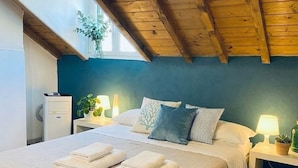 Een slaapkamer met een houten plafond, een bed met witte lakens, twee nachtkastjes met lampen en een raam met een plant.