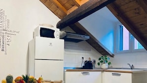 Een keuken met een witte koelkast, een magnetron, een spoelbak en een raam met uitzicht.