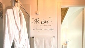 Een badkamer met een witte badjas, een handdoekhouder met een handdoek, en een bordje met de tekst 'Ontspan, neem een lange, hete douche en laat je zorgen wegwassen'.