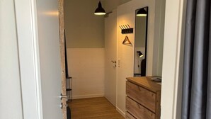 Ein Flur mit Holzboden, Holzbalkendecke, einer Pendelleuchte, einem Spiegel und einer hölzernen Kommode.