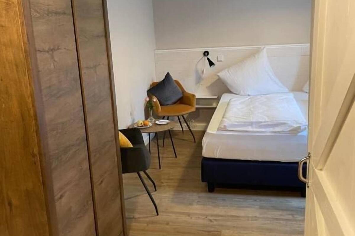 Ein Hotelzimmer mit einem Bett, einem Holzschrank, einem kleinen Tisch mit Stuhl und einer Hängelampe.