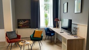 Ein modernes Wohnzimmer mit einer Couch, Sesseln, einem Couchtisch, einem Fernseher und Kunstwerken an der Wand.