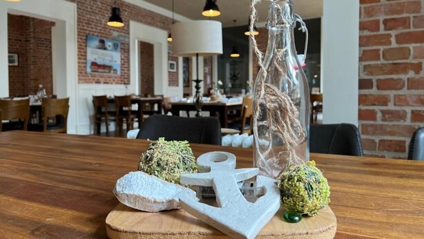 Ein Holztisch mit dekorativen Gegenständen, darunter eine Glasflasche, ein Anker und zwei runde Objekte.
