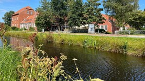 Blick auf einen Fluss mit einem Gebäude aus roten Ziegelsteinen, Bäumen und ruhigem Wasser.