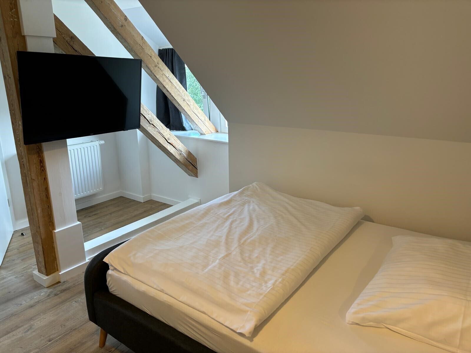 Een slaapkamer met een bed, een raam met uitzicht en een aan de muur bevestigde televisie.