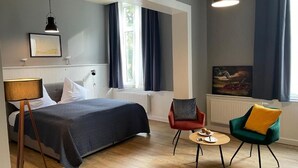 Ein Hotelzimmer mit Bett, Schreibtisch, zwei Stühlen, einer Lampe und einem Bild an der Wand.