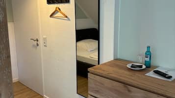 A bedroom with a wooden dresser, a hanging coat rack, a bed, and a mirror.