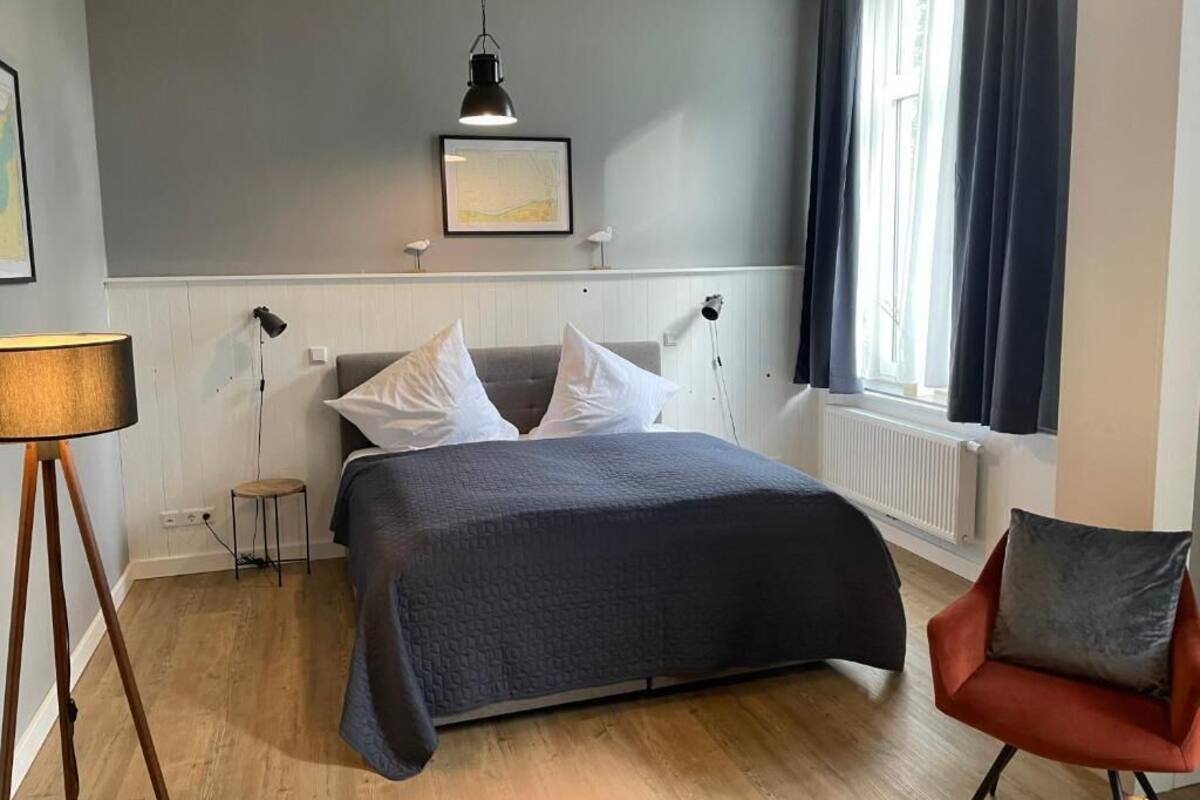 Ein Schlafzimmer mit einem Bett, einem Sessel, einer Lampe und einem Fenster.