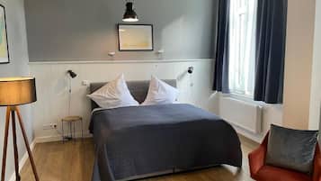 A bedroom with a bed, a chair, a lamp, and a window.