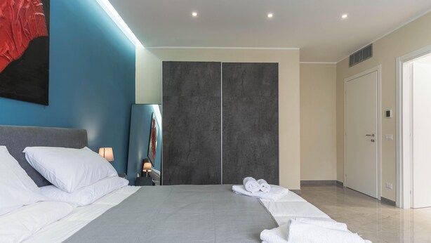 Ein modernes Schlafzimmer mit einem großen Bett, einem Kleiderschrank, einem Spiegel und einem roten, abstrakten Gemälde an der Wand.
