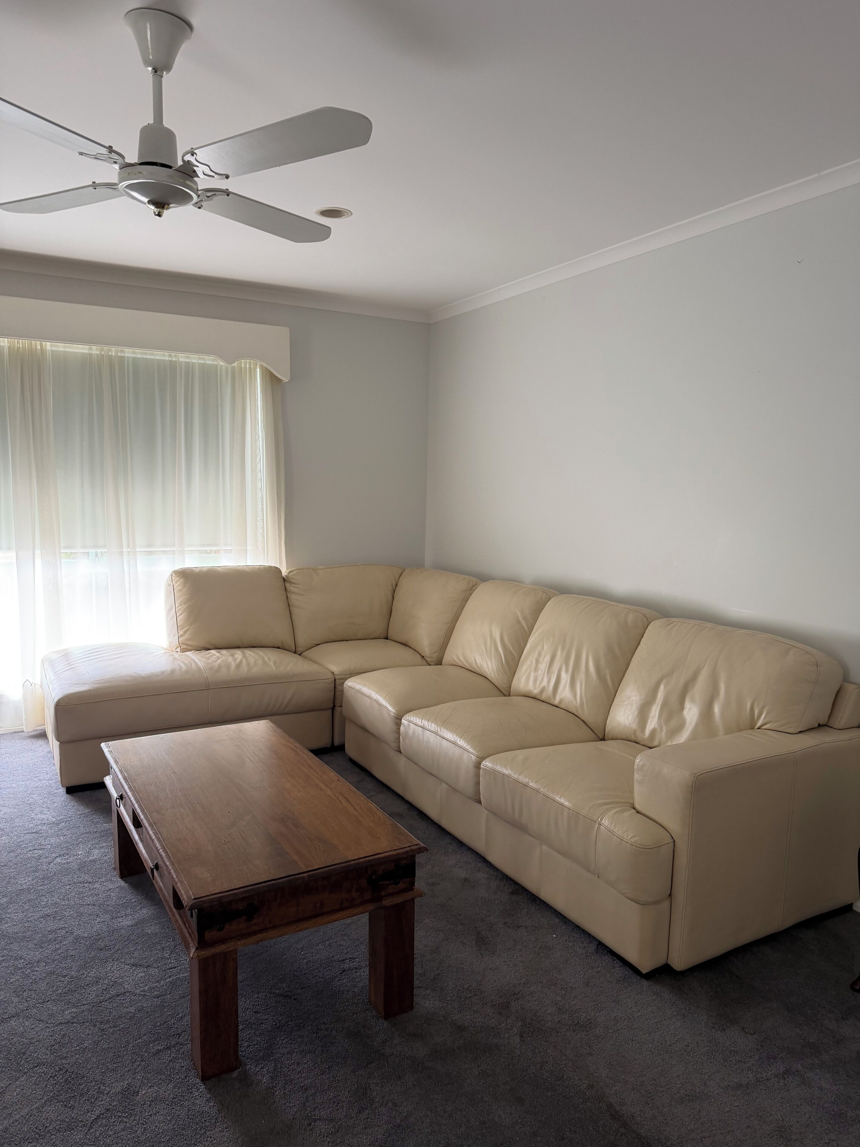 A living room with a sectional sofa, a wooden coffee table, and a ceiling fan.