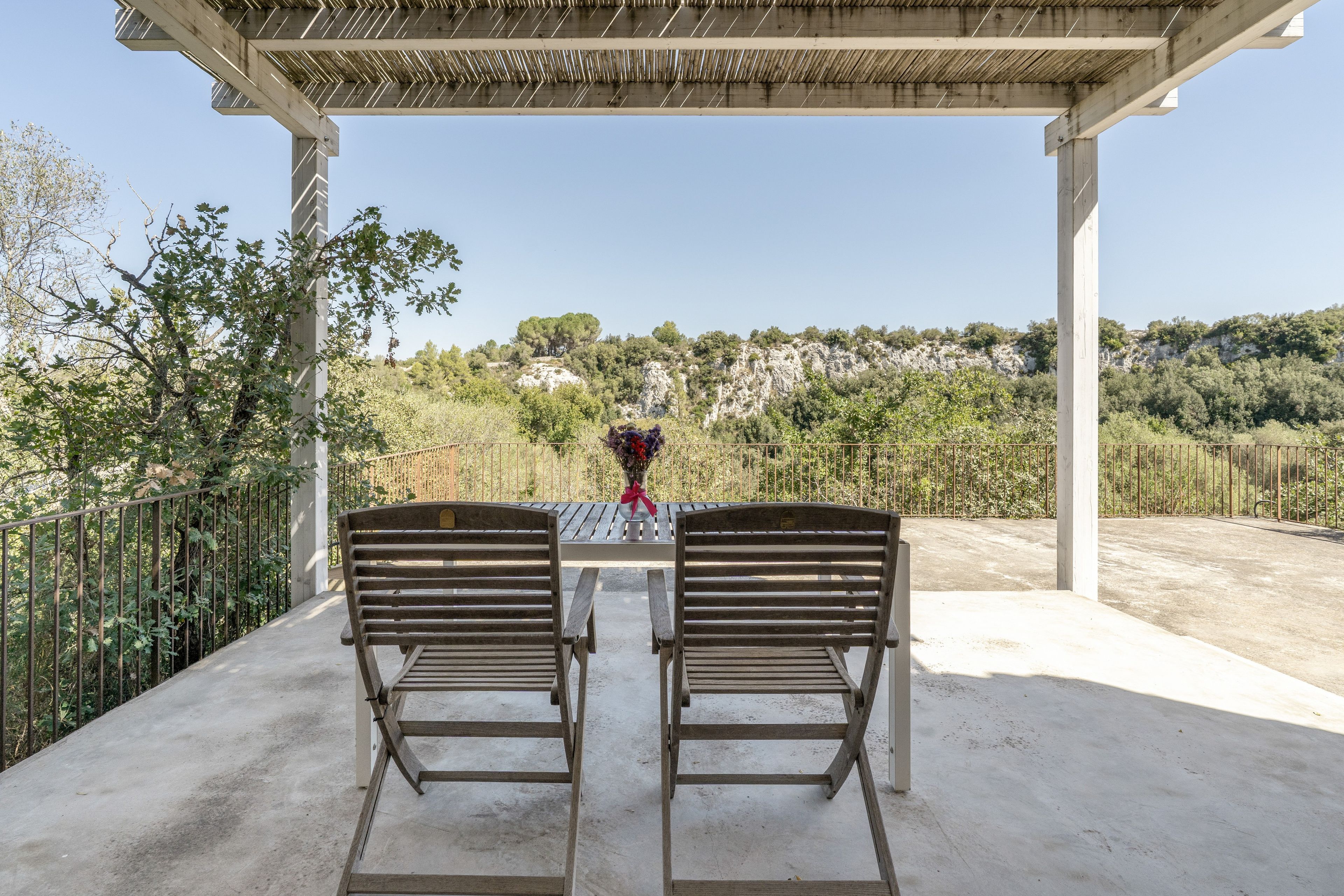 An outdoor seating area with two wooden benches under a pergola, overlooking a mountainous landscape.