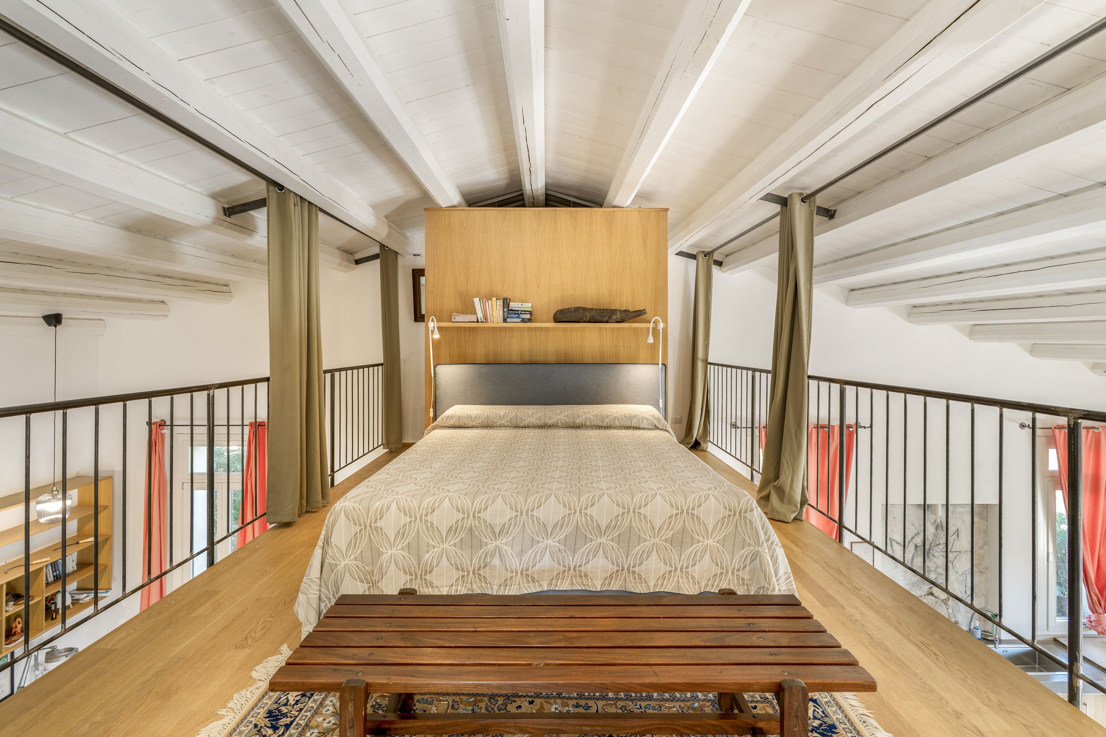 A high-ceilinged room with a bed, a wooden bench, and a bookshelf.