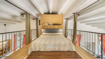 A high-ceilinged room with a bed, a wooden bench, and a bookshelf.