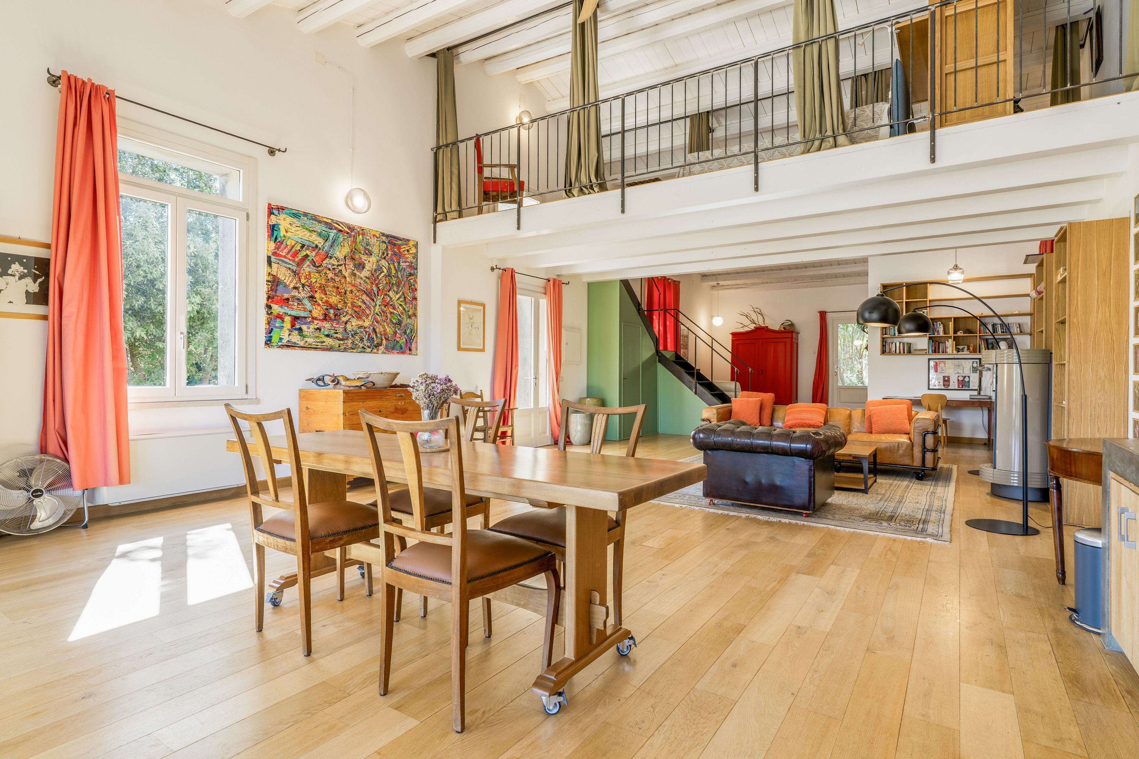 A spacious living area with a dining table, chairs, a sofa, and a staircase leading to an upper level.