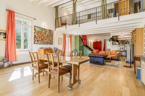 A spacious living area with a dining table, chairs, a sofa, and a staircase leading to an upper level.