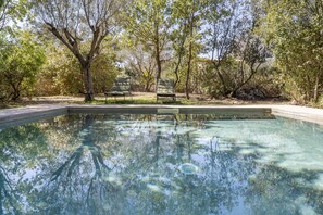A clear swimming pool with two chairs and a stone wall in the background.