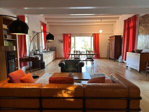 A living room with a leather sofa, a dining table with chairs, a kitchen area, and red curtains. - Villa Manghisi with Private Pool, Wi-Fi and Air Conditioning (Noto)