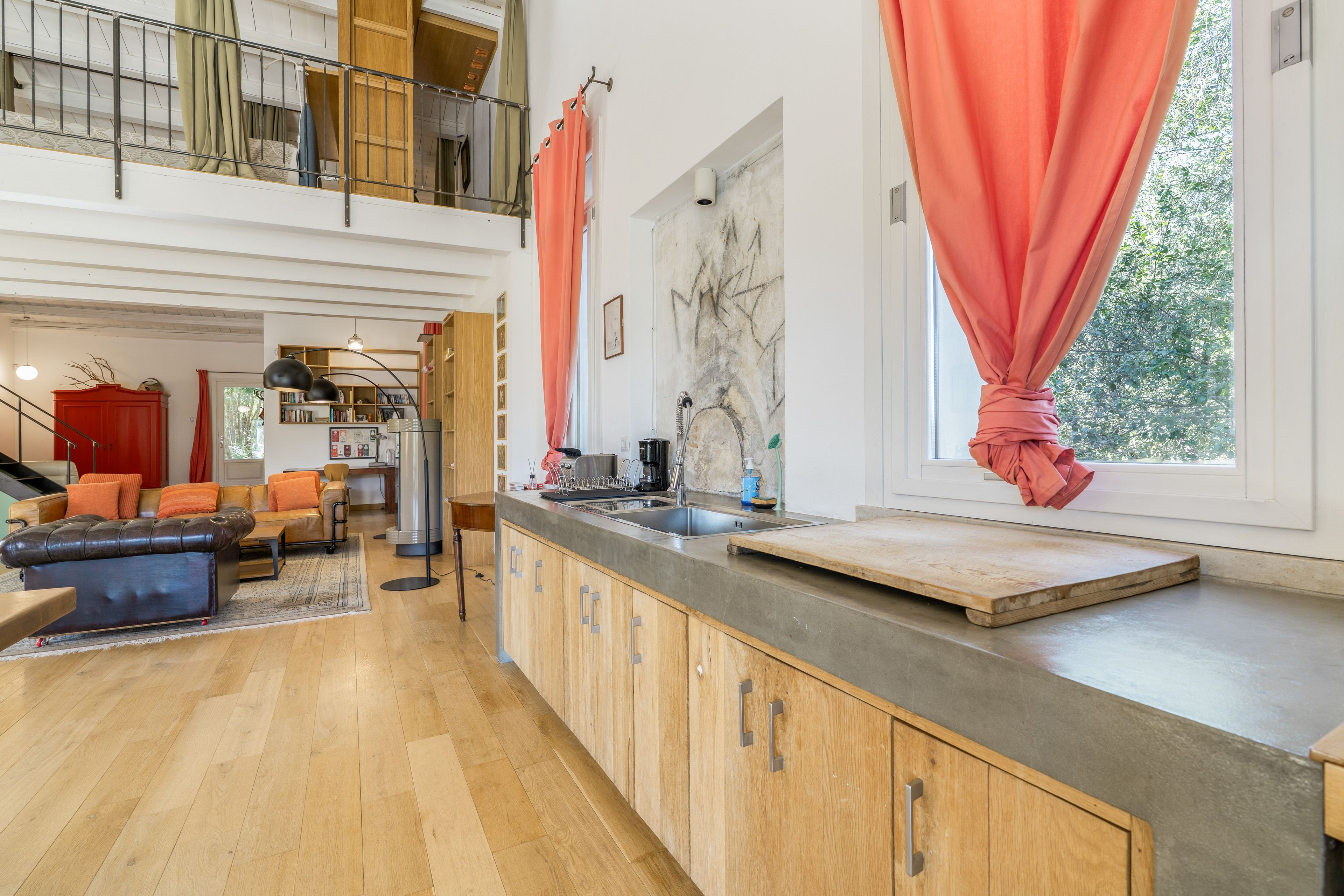 Une cuisine moderne dotée d’un grand îlot central, de meubles en bois et offrant une vue sur l’extérieur grâce à une fenêtre.