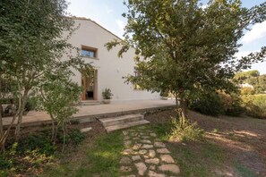 A white building with a stone pathway leading to a wooden door, surrounded by greenery. - Villa Manghisi with Private Pool, Wi-Fi and Air Conditioning (Noto)