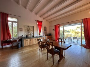 A spacious kitchen with wooden cabinets, a dining area with a table and chairs, and large windows with red curtains. - Villa Manghisi with Private Pool, Wi-Fi and Air Conditioning (Noto)