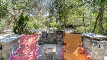 An outdoor seating area with two chairs and a table, surrounded by trees and a stone wall.