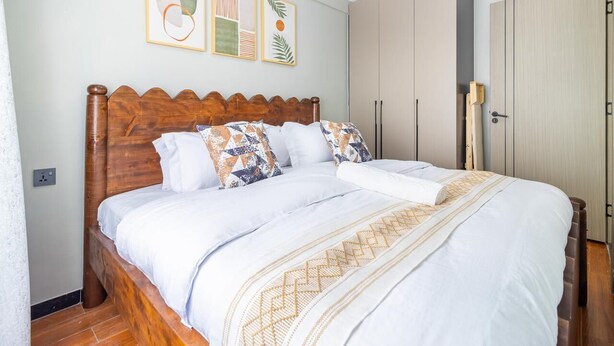 A neatly made bed with a wooden headboard, a white comforter, and patterned pillows. There are framed artworks on the wall above the bed. - VEE LUX BNB

Thindigua Finest (Nairobi)