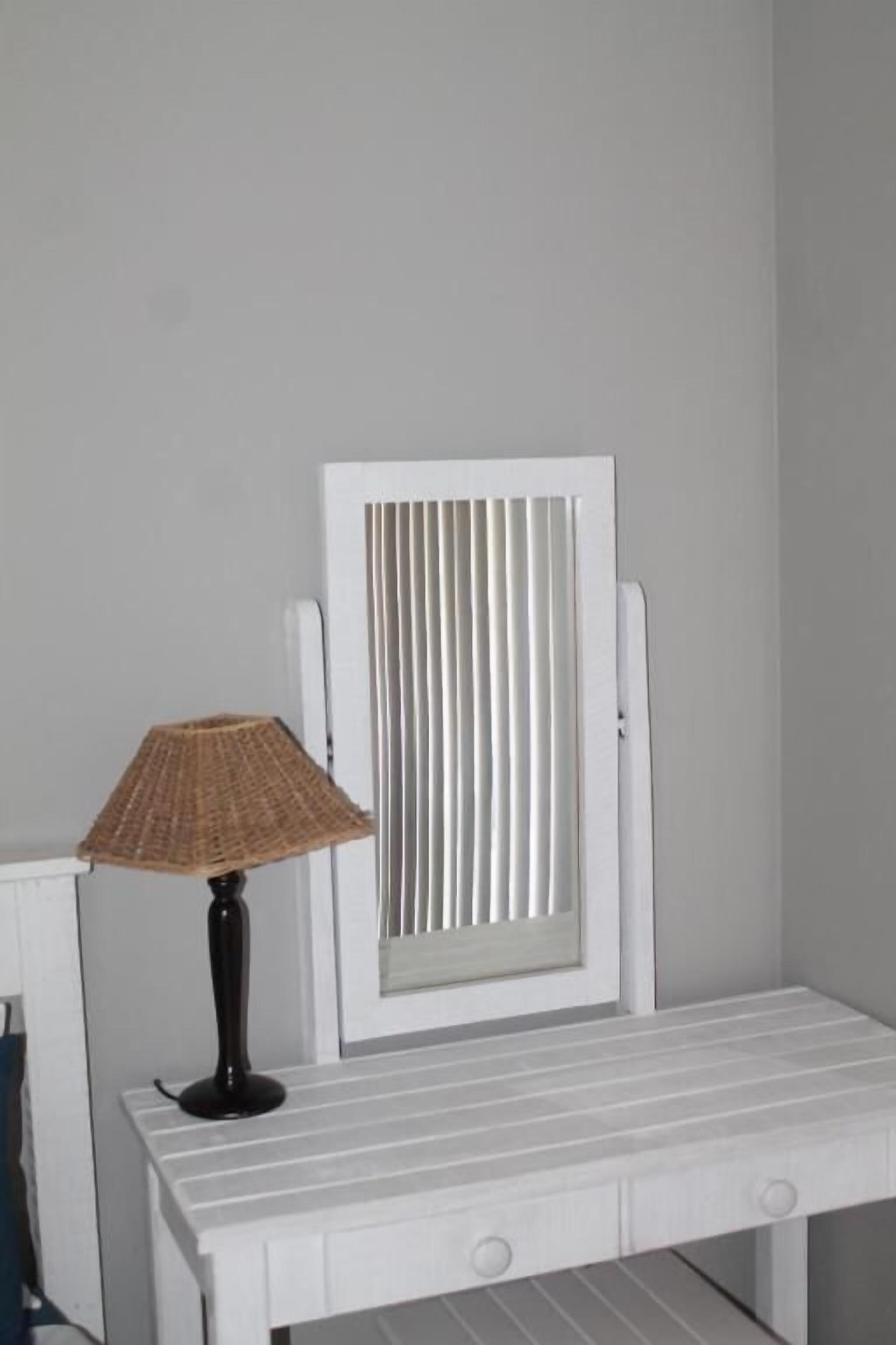 Une table de chevet blanche, avec une lampe, un miroir et un radiateur.