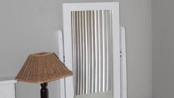 Une table de chevet blanche, avec une lampe, un miroir et un radiateur.